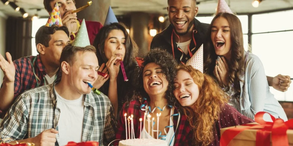 Grupo de amigos celebrando un cumpleaños con sombreros de fiesta, velas en un pastel y sonrisas, disfrutando de un momento especial juntos.