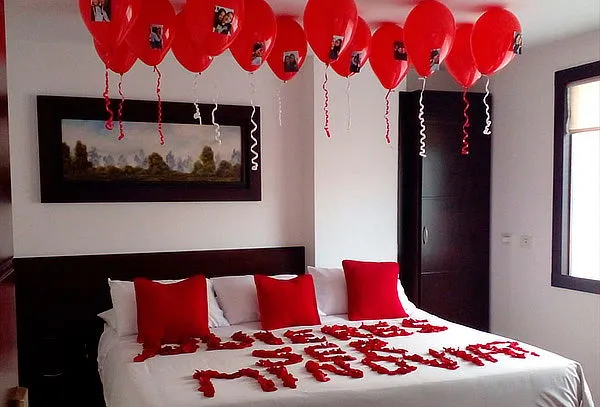 Decoración romántica en una habitación con globos rojos y pétalos de rosa en la cama